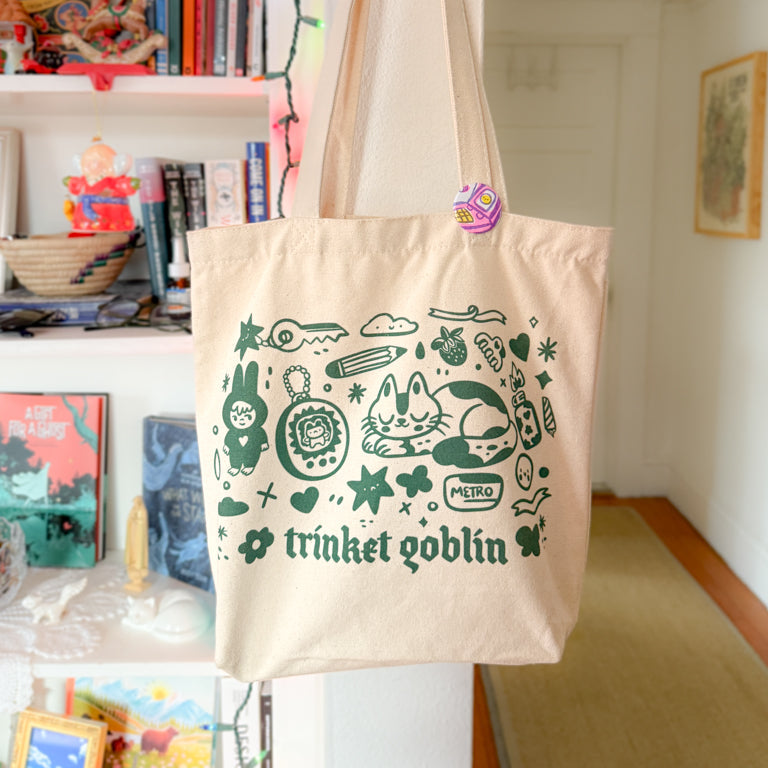 Beige tote bag with green graphics and text hanging on a hook in a room.